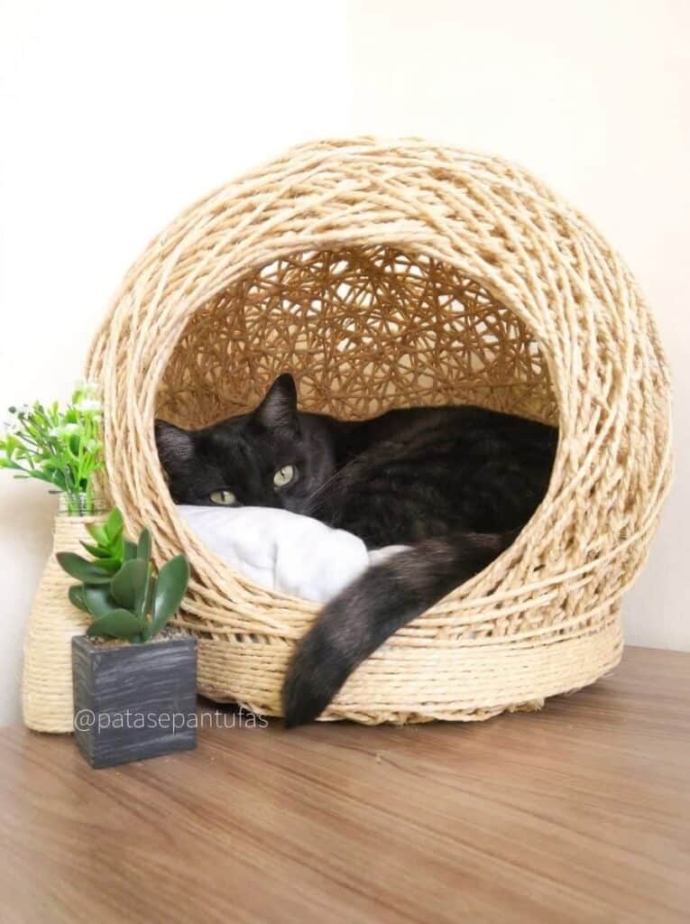Gato preto descansando dentro de uma toca artesanal para gatos em sisal.